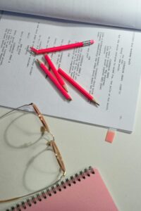 Still life of a workspace with pink pencils, papers, and glasses on a desk.